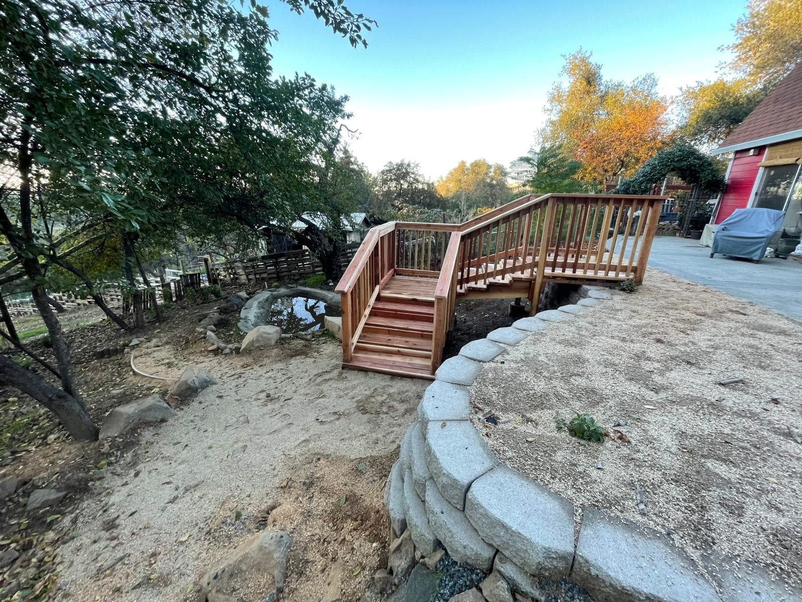 Custom redwood staircase with railing and landing beside a curved segmental block retaining wall on a graded slope